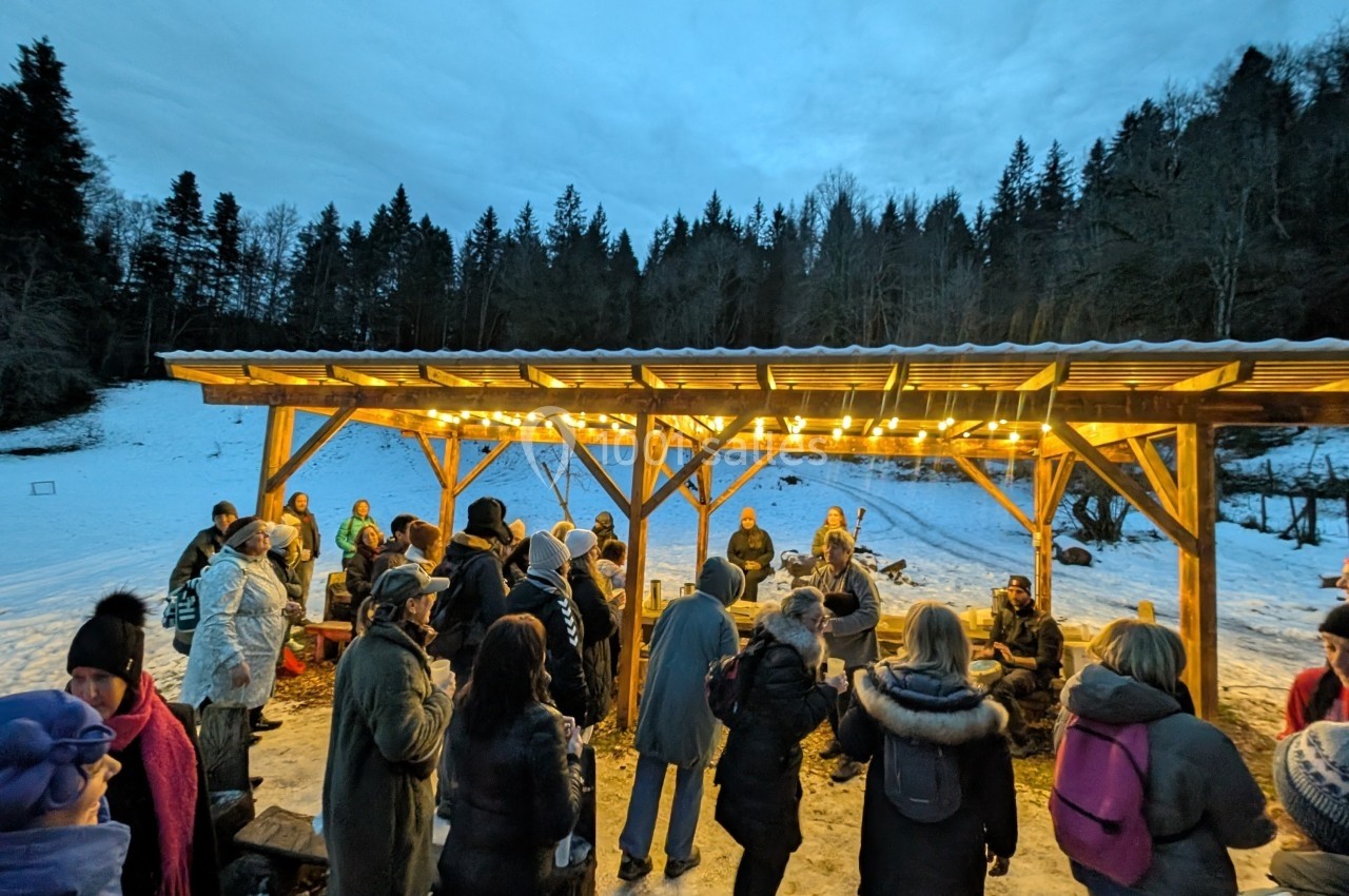 Location salle Crozets (Jura) - Domaine Le Coupet #25 Groupe de personnes rassemblées sous un abri éclairé en bois, entouré de neige et d'arbres en arrière-plan.