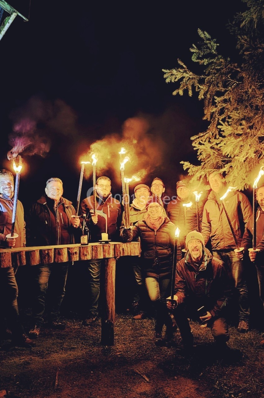 Location salle Crozets (Jura) - Domaine Le Coupet #26 Un groupe de personnes tenant des torches allumées, rassemblées dehors la nuit près d'une cabane en bois.