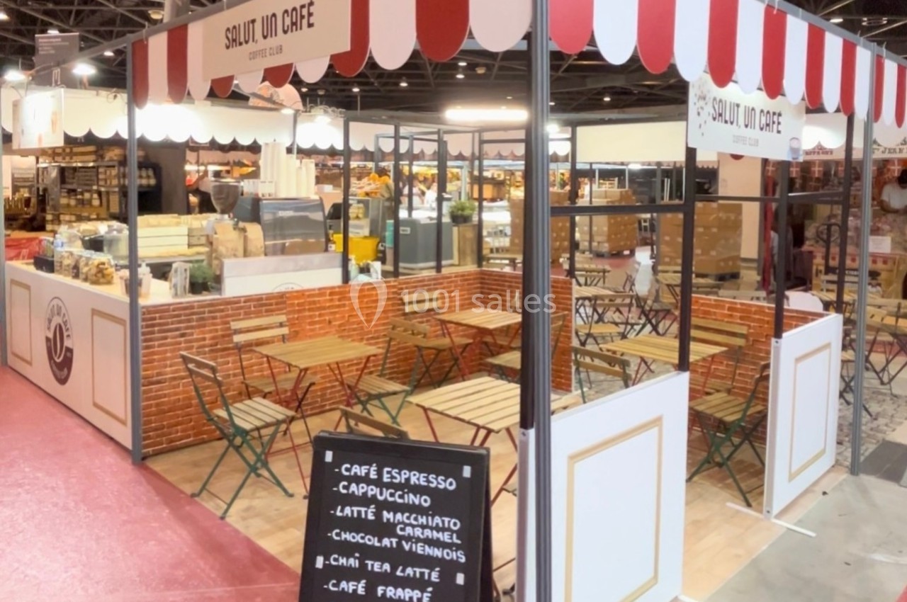 Stand de café avec terrasse aménagée, tables et chaises, menu sur ardoise indiquant boissons et spécialités.