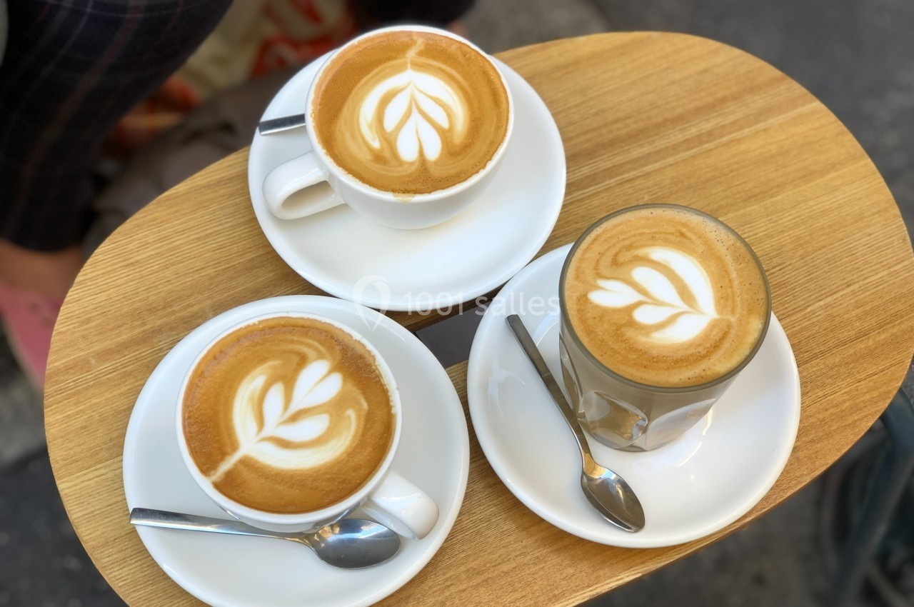 Trois boissons au café avec latte art en forme de feuilles, servies sur une table en bois avec des cuillères.