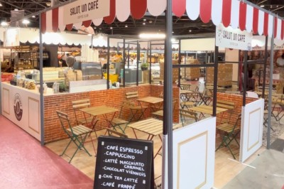 Camionnette de café avec une porte ouverte, stationnée dans un espace extérieur bordé d'arbres et de stands.