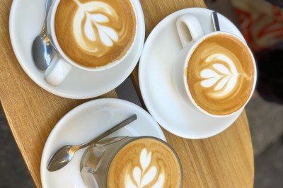 Camionnette de café avec une porte ouverte, stationnée dans un espace extérieur bordé d'arbres et de stands.
