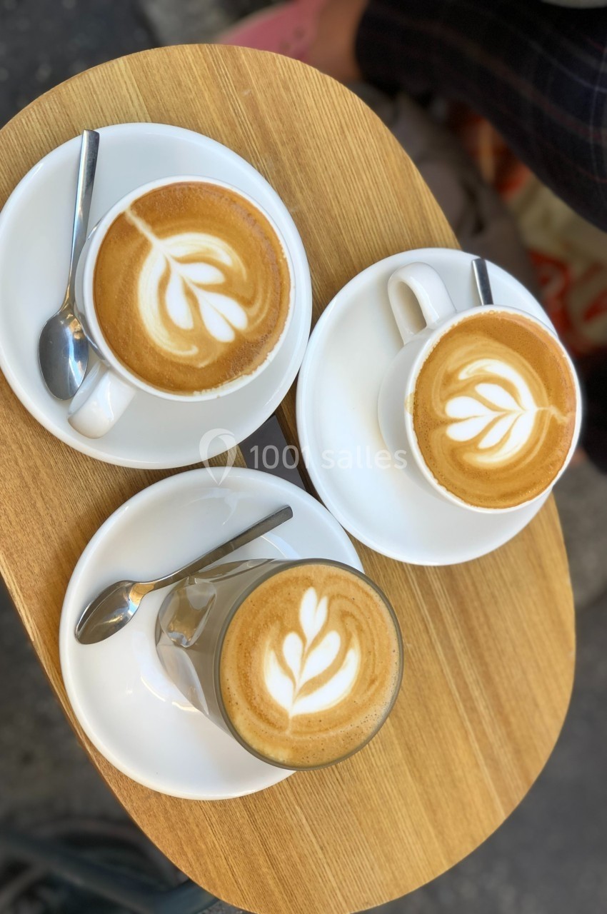 Trois boissons au café avec latte art en forme de feuille, servies sur une table en bois avec des cuillères.