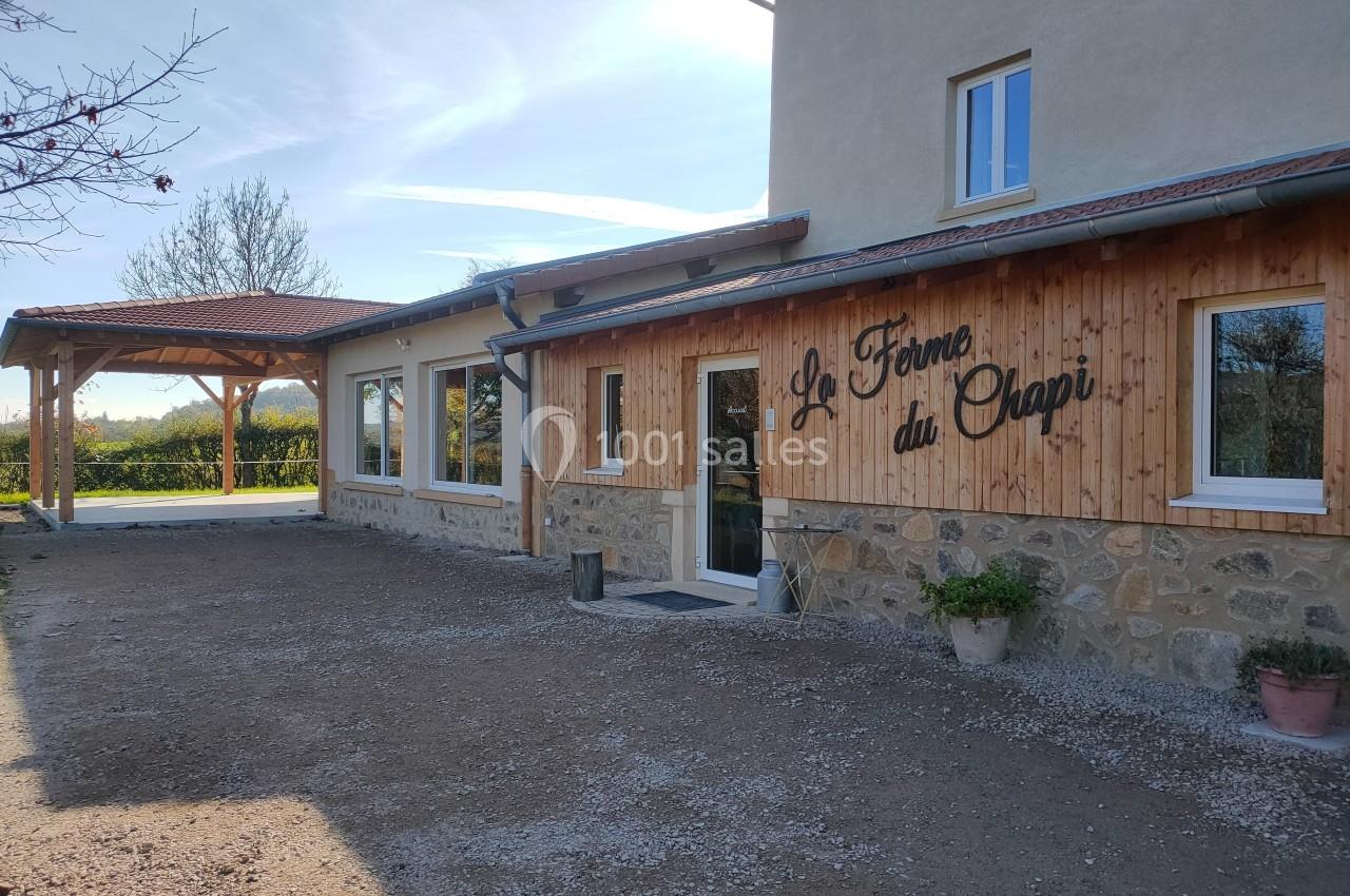 Façade d'un bâtiment en pierre et bois avec l'inscription ’La Ferme du Chapi’, entouré d'un espace extérieur dégagé.