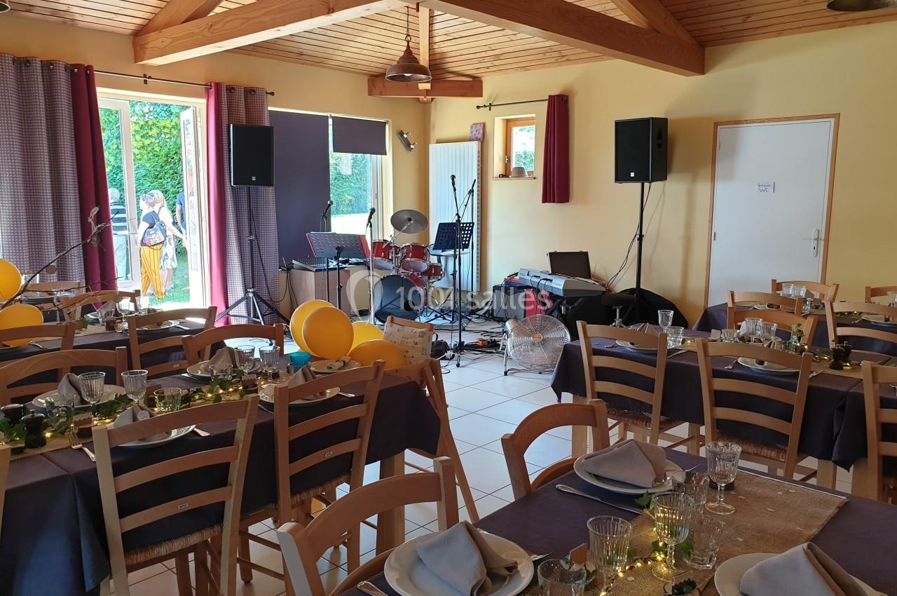 Salle décorée pour un événement avec tables dressées, instruments de musique et matériel audio en arrière-plan.