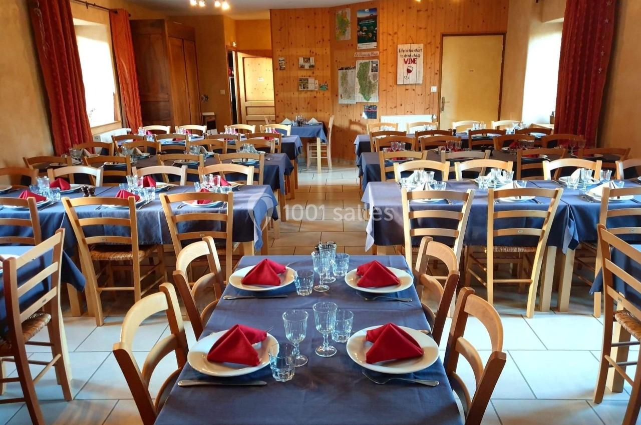 Salle de restaurant avec tables dressées, nappes bleues, serviettes rouges pliées et chaises en bois.