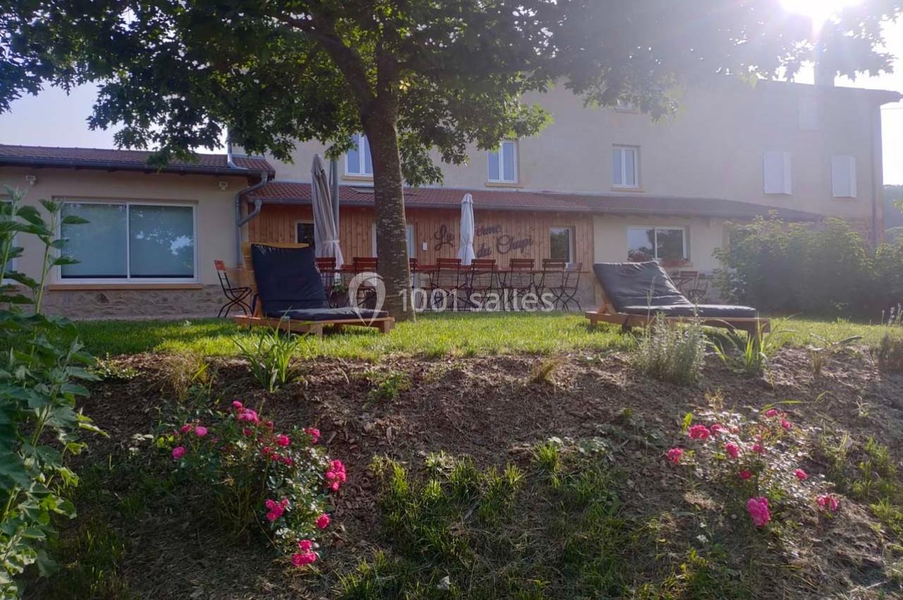 Façade d'un bâtiment avec terrasse aménagée, chaises longues sur une pelouse et fleurs au premier plan.