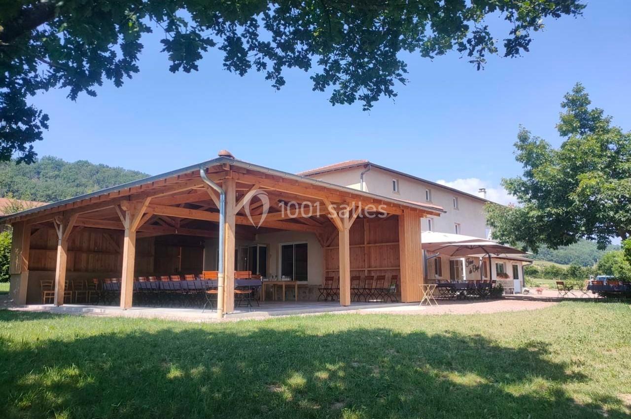 Structure en bois ouverte avec tables et chaises, située dans un espace verdoyant sous un ciel dégagé.