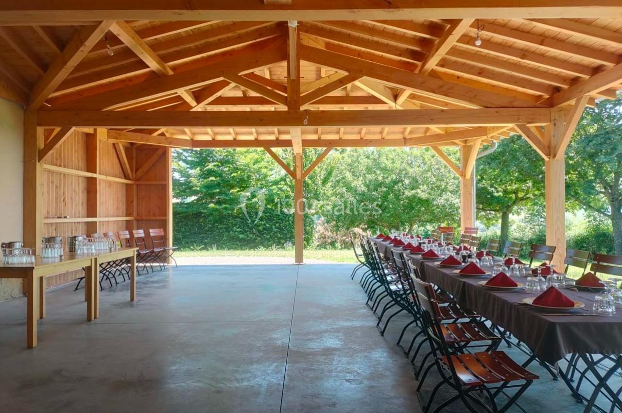 Salle en bois ouverte avec tables dressées et chaises alignées, donnant sur un jardin verdoyant en arrière-plan.