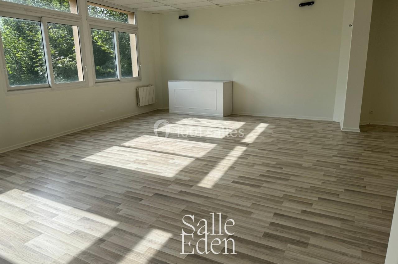 Salle vide avec parquet clair, murs blancs, plafond à dalles et grandes fenêtres laissant entrer la lumière naturelle.