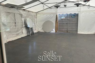 Salle vide avec parquet sombre, murs en bois, fauteuils noirs, tables basses, et une boule disco suspendue au plafond.