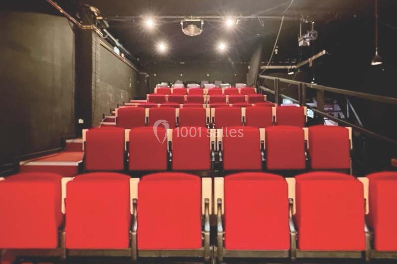 Salle de spectacle avec des rangées de sièges rouges vides et un éclairage tamisé.