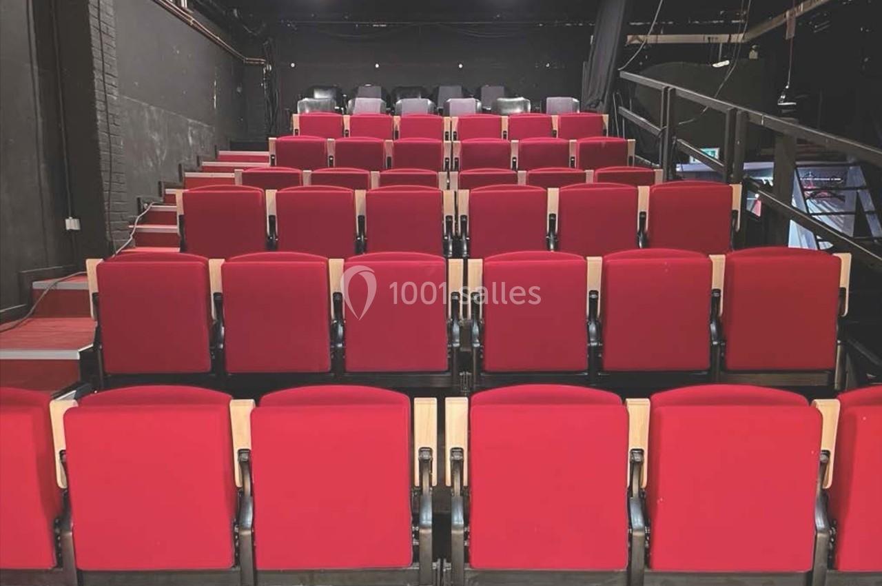 Salle de spectacle avec des rangées de sièges rouges vides et une scène visible en arrière-plan.
