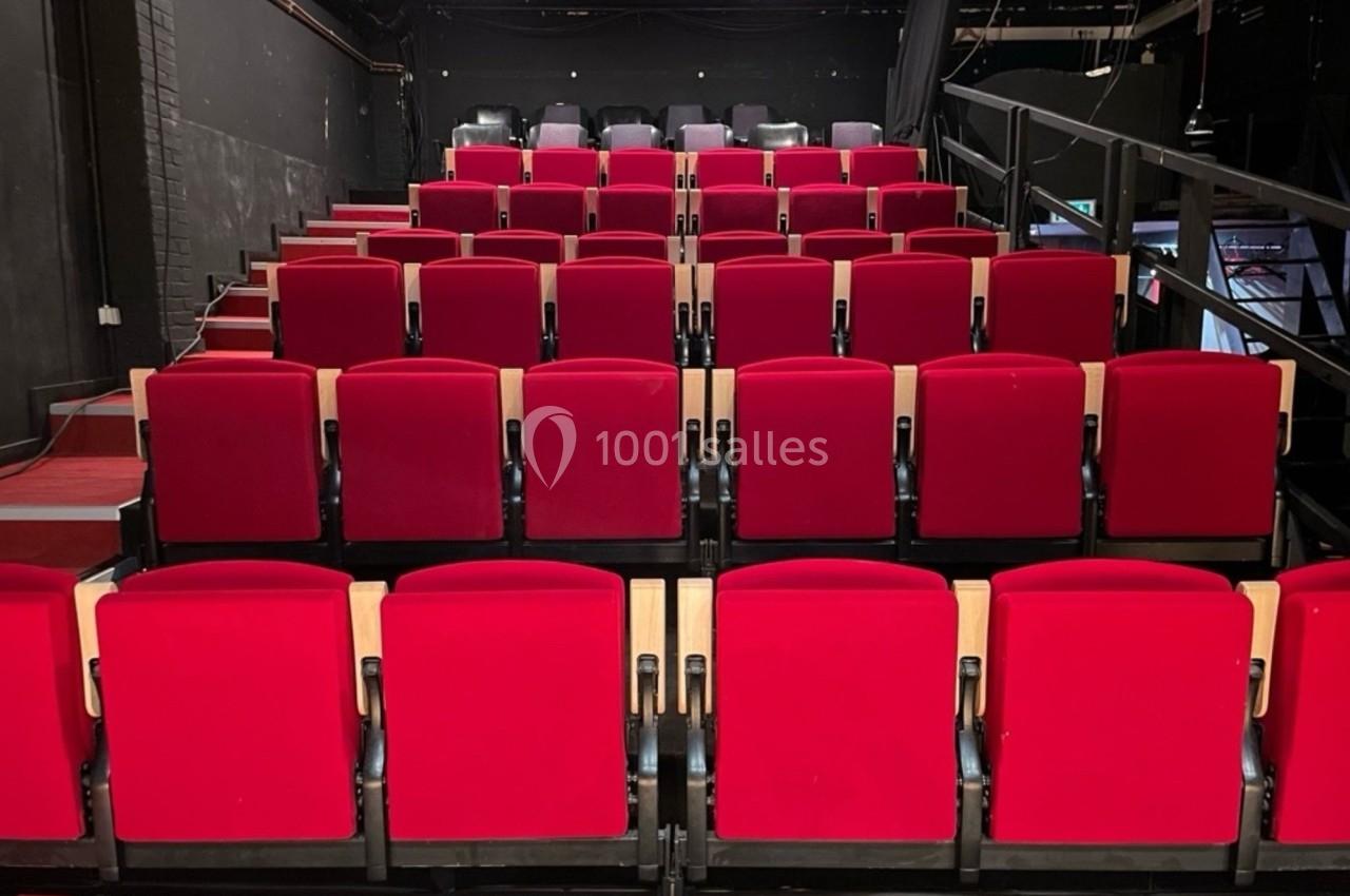Rangées de fauteuils rouges alignés dans une petite salle de spectacle ou de théâtre.