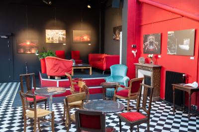 Espace salon avec canapés et fauteuils rouges, table basse en bois, plantes et photos encadrées sur un mur sombre.