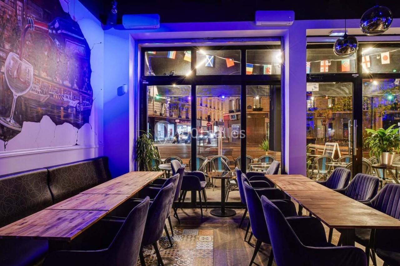 Salle de restaurant moderne avec tables en bois, chaises rembourrées et vue sur une rue animée à travers de grandes baies…