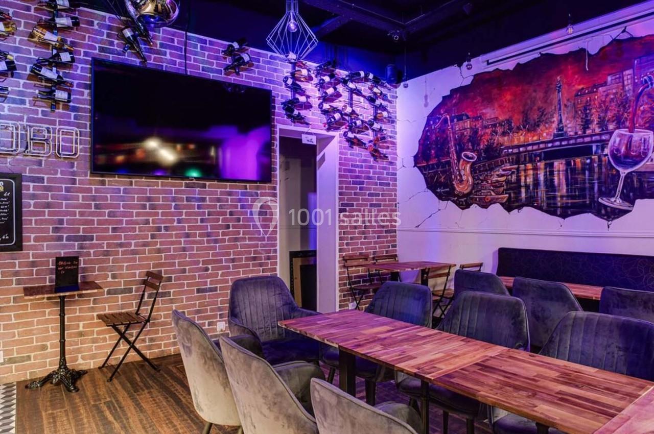 Salle de restaurant avec murs en briques, tables en bois, chaises rembourrées et éclairage violet.