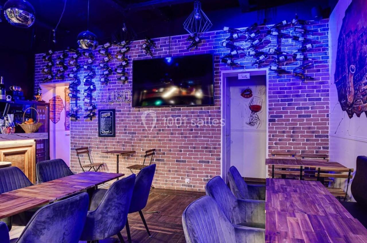 Salle de restaurant avec murs en briques, tables en bois, chaises rembourrées et éclairage tamisé bleu.