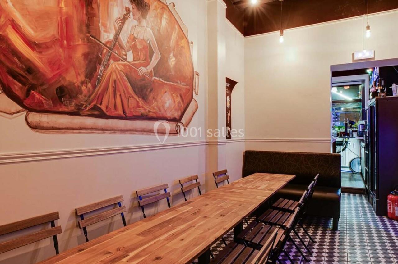 Salle avec une longue table en bois, chaises, fresque murale colorée et sol en carrelage noir et blanc.