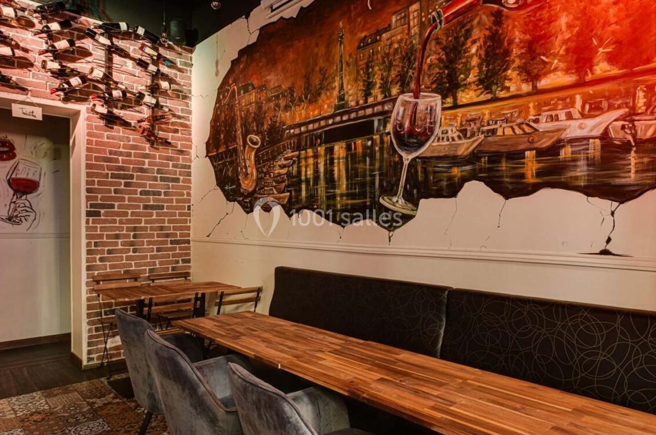 Mur décoré d'une fresque représentant un paysage urbain avec des verres de vin, tables et chaises en bois au premier plan.