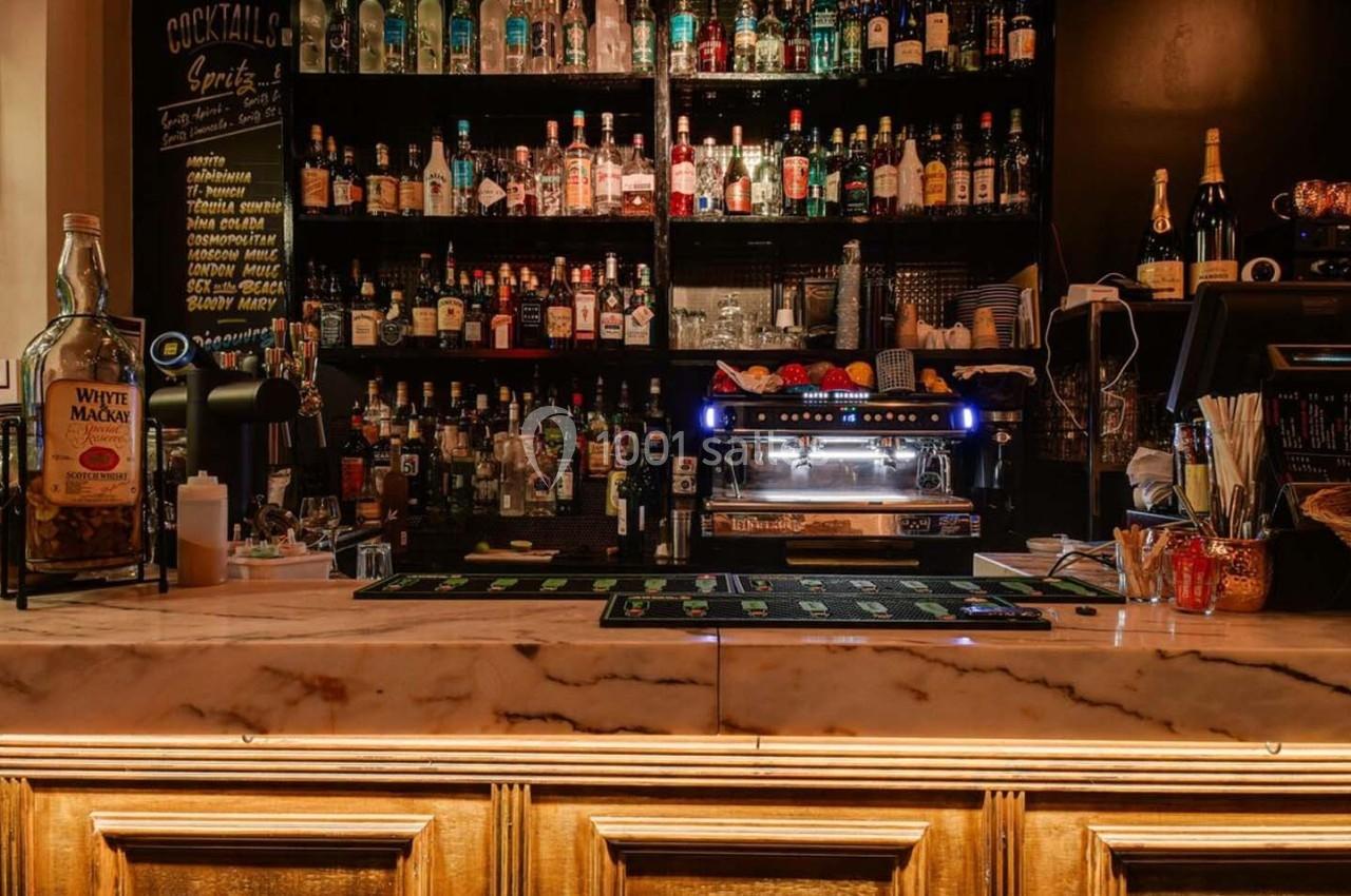 Comptoir de bar en marbre avec bouteilles d'alcool en arrière-plan, machine à café et corbeille de fruits.