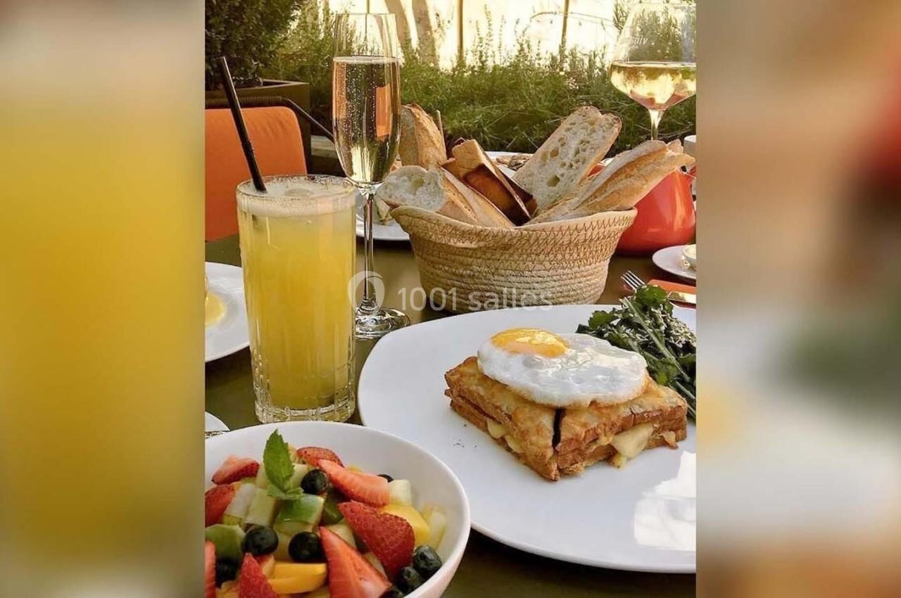 Assiette avec croque-madame, salade de fruits, jus d'orange, pain et verres de vin sur une table en extérieur.