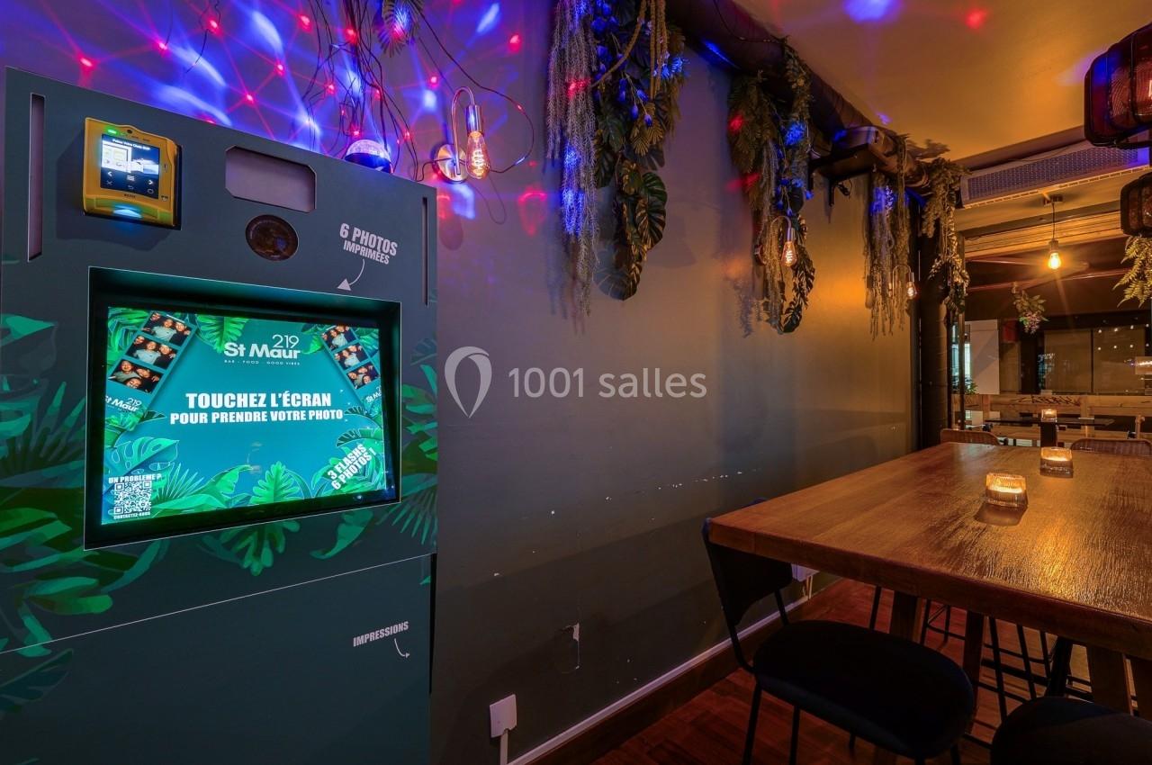 Borne photo interactive dans un espace intérieur décoré de plantes suspendues et éclairages colorés.