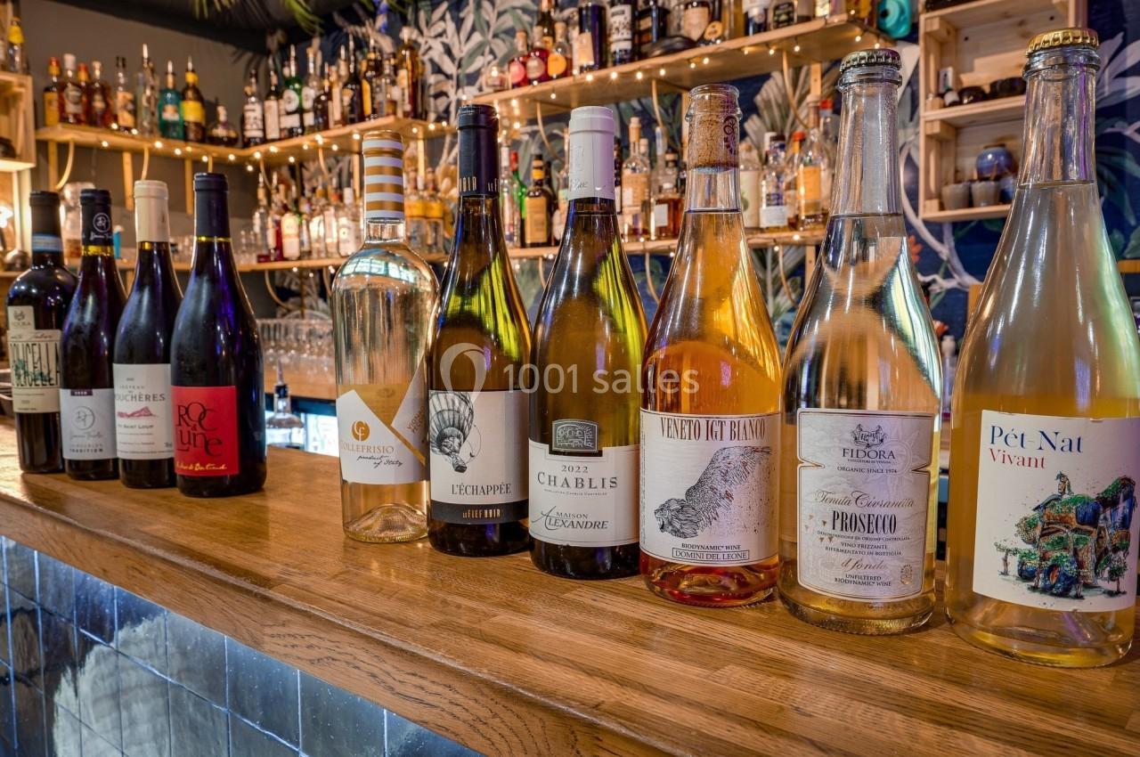 Une rangée de bouteilles de vin variées alignées sur un comptoir en bois, avec un bar en arrière-plan.