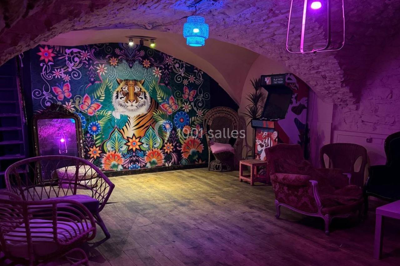 Salle voûtée décorée avec un mur coloré représentant un tigre entouré de fleurs, mobilier vintage et éclairage tamisé.
