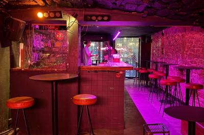 Salle sombre avec un comptoir à gauche, un sol en béton éclairé par des lumières colorées et une sortie illuminée au fond.