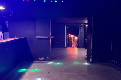 Salle sombre avec un comptoir à gauche, un sol en béton éclairé par des lumières colorées et une sortie illuminée au fond.