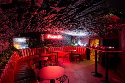 Miniature Bar Principal Salle voûtée en pierre avec un comptoir rouge, éclairage chaleureux et escalier menant à un rideau rouge.