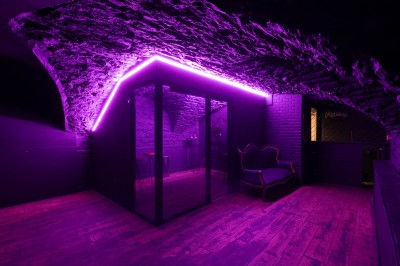 Salle voûtée en pierre avec un comptoir rouge, éclairage chaleureux et escalier menant à une ouverture avec rideau rouge.