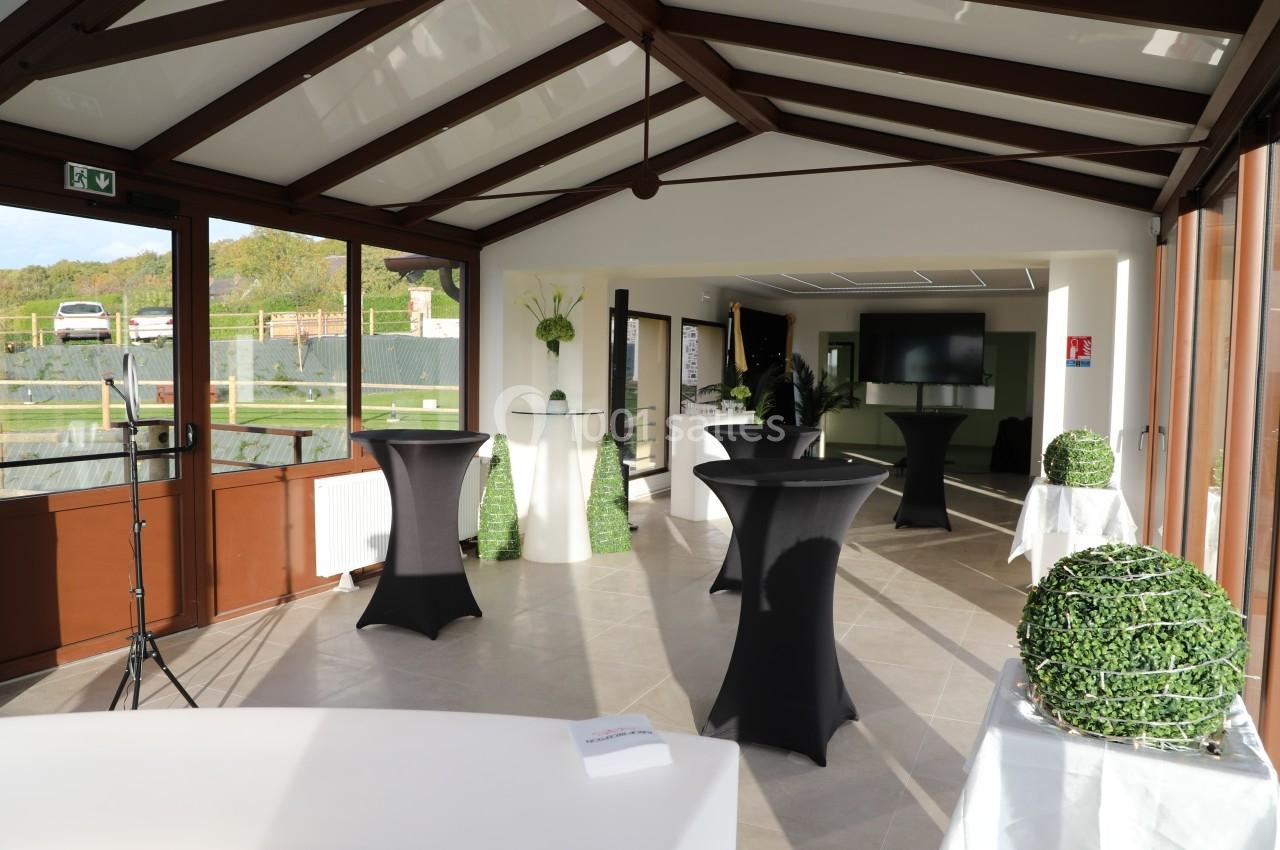 Location salle Saint-Samson-de-la-Roque (Eure) - Manoir Néo Normand #10 Salle lumineuse avec tables hautes noires, décorations végétales et grandes baies vitrées donnant sur l'extérieur.