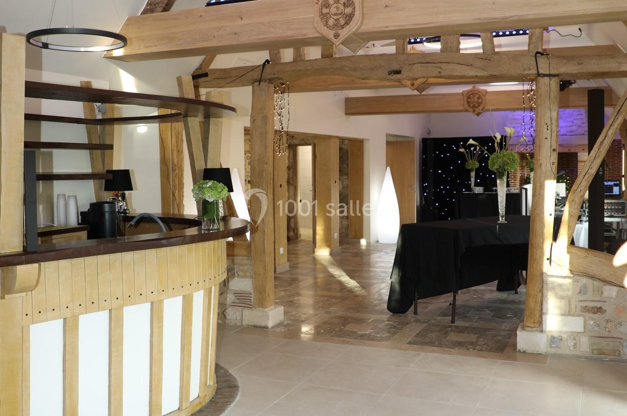 Location salle Saint-Samson-de-la-Roque (Eure) - Manoir Néo Normand #11 Intérieur d'une salle de réception avec poutres apparentes, comptoir en bois et tables décorées de fleurs.