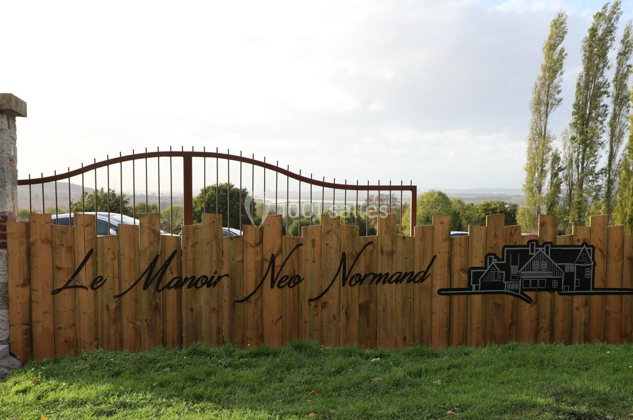 Location salle Saint-Samson-de-la-Roque (Eure) - Manoir Néo Normand #25 Clôture en bois avec le texte ’Le Manoir Néo Normand’ et un dessin de manoir, sur fond de paysage rural.