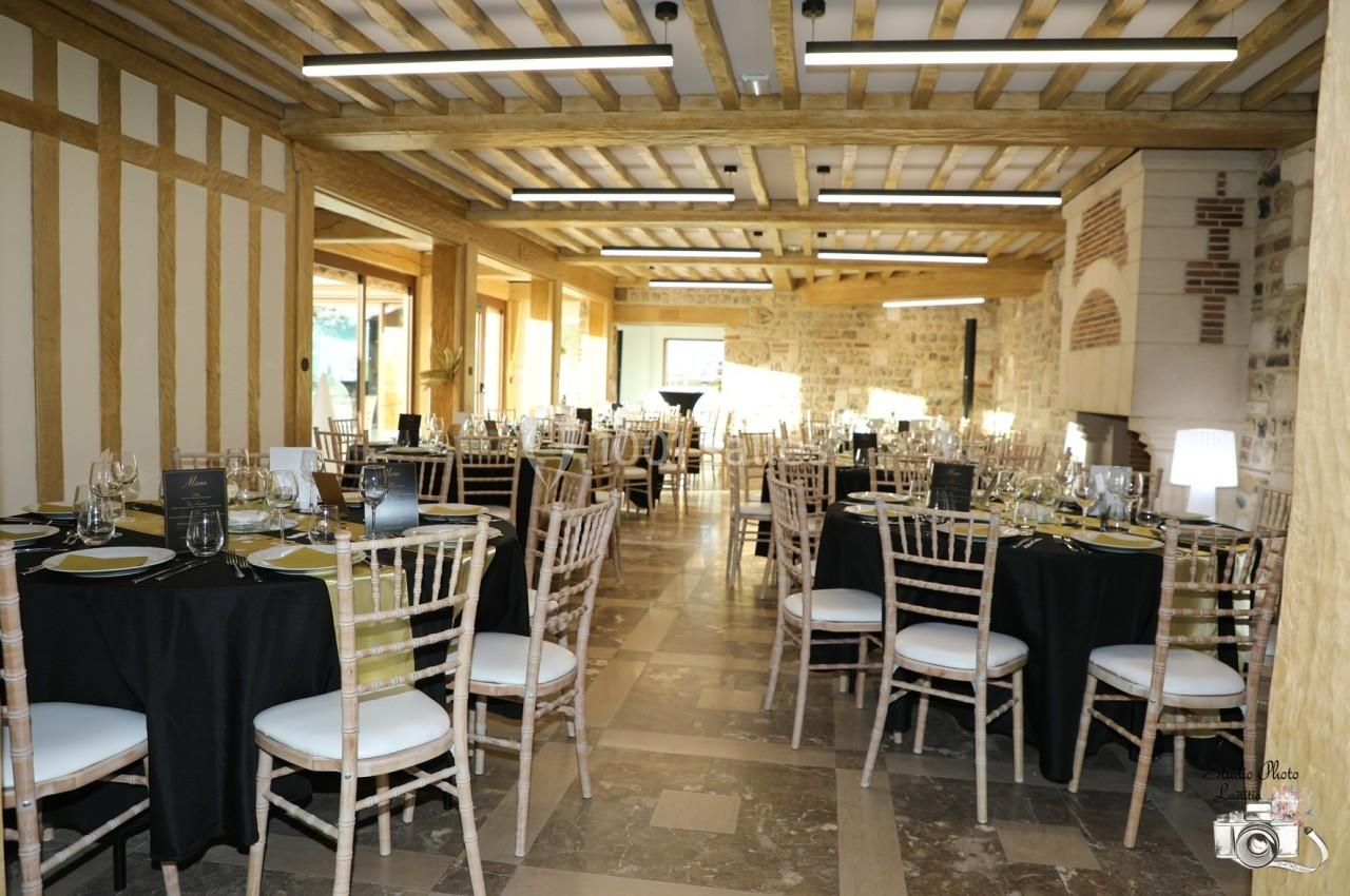 Location salle Saint-Samson-de-la-Roque (Eure) - Manoir Néo Normand #32 Salle de réception lumineuse avec tables dressées, nappes noires et chaises en bois, dans un décor rustique en pierre et…