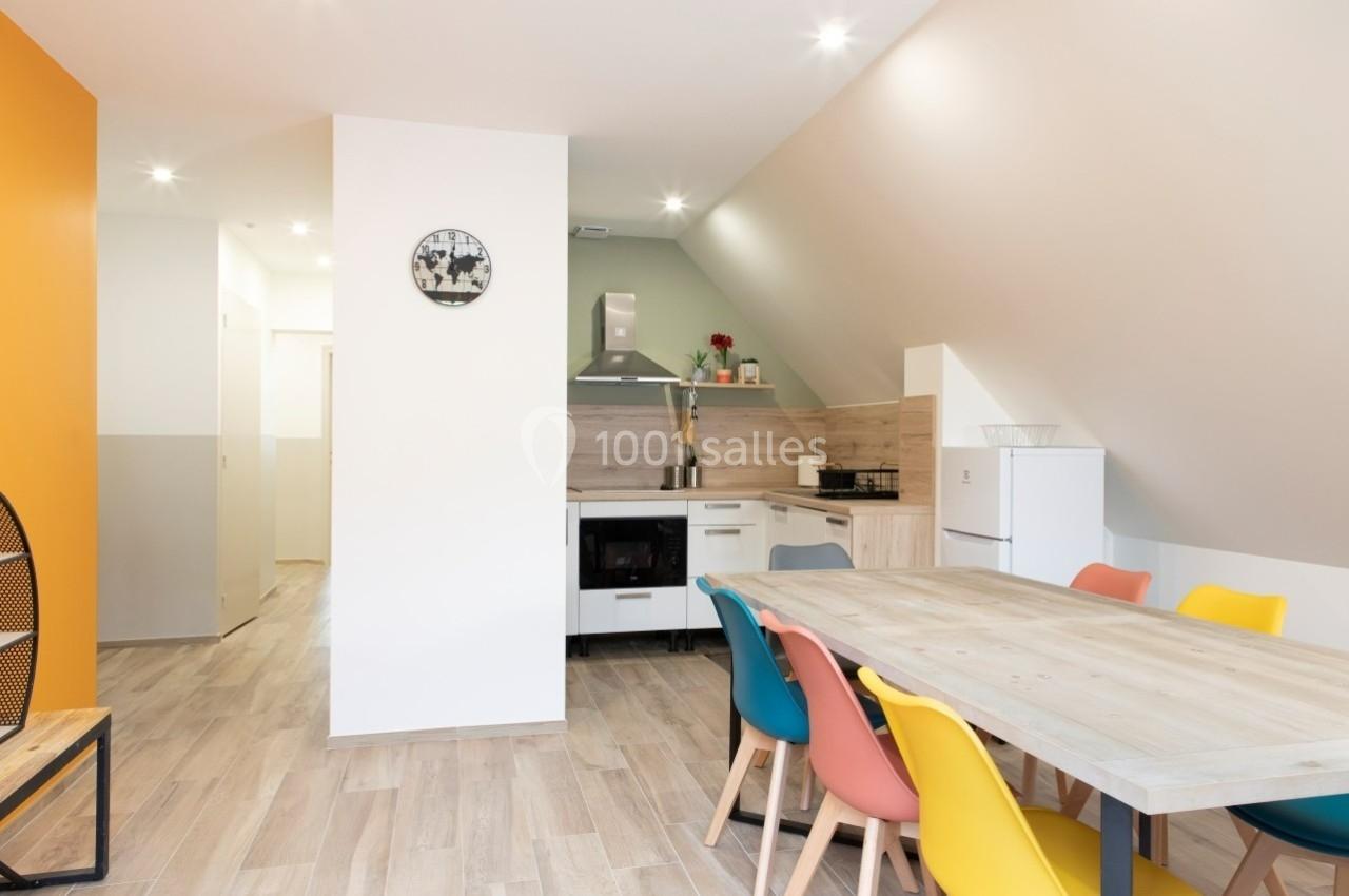 Location salle Saint-Samson-de-la-Roque (Eure) - Manoir Néo Normand #35 Salle à manger lumineuse avec table en bois, chaises colorées et cuisine ouverte équipée en arrière-plan.