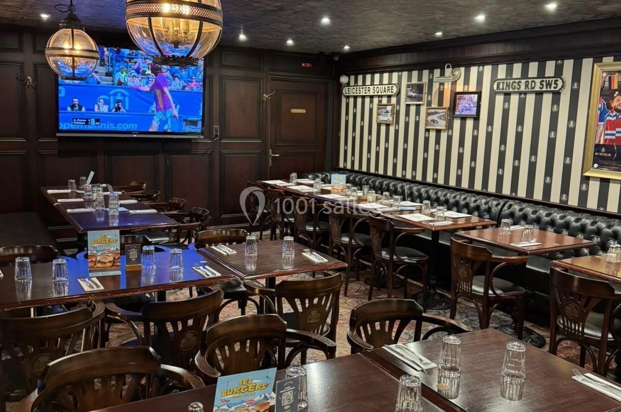 Salle de restaurant avec tables en bois dressées, banquettes noires, décor rétro et télévision diffusant un match.