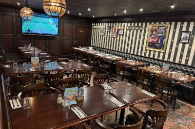 Salle de restaurant avec tables en bois dressées, banquettes noires, murs rayés et écran diffusant un match de tennis.
