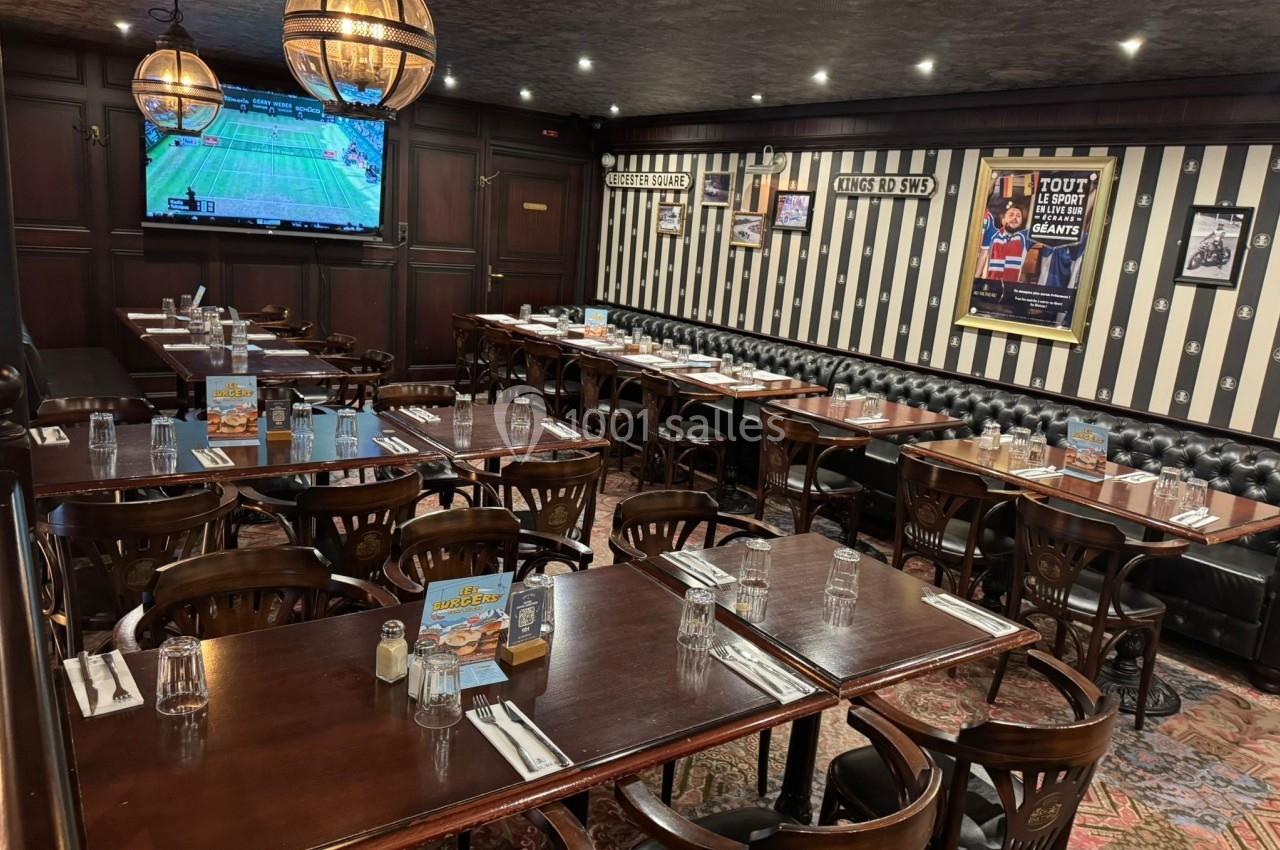Salle de restaurant avec tables en bois dressées, banquettes noires, murs rayés et écran diffusant un match de tennis.