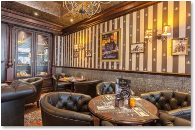 Salle de restaurant avec tables en bois dressées, banquettes noires, murs rayés et écran diffusant un match de tennis.