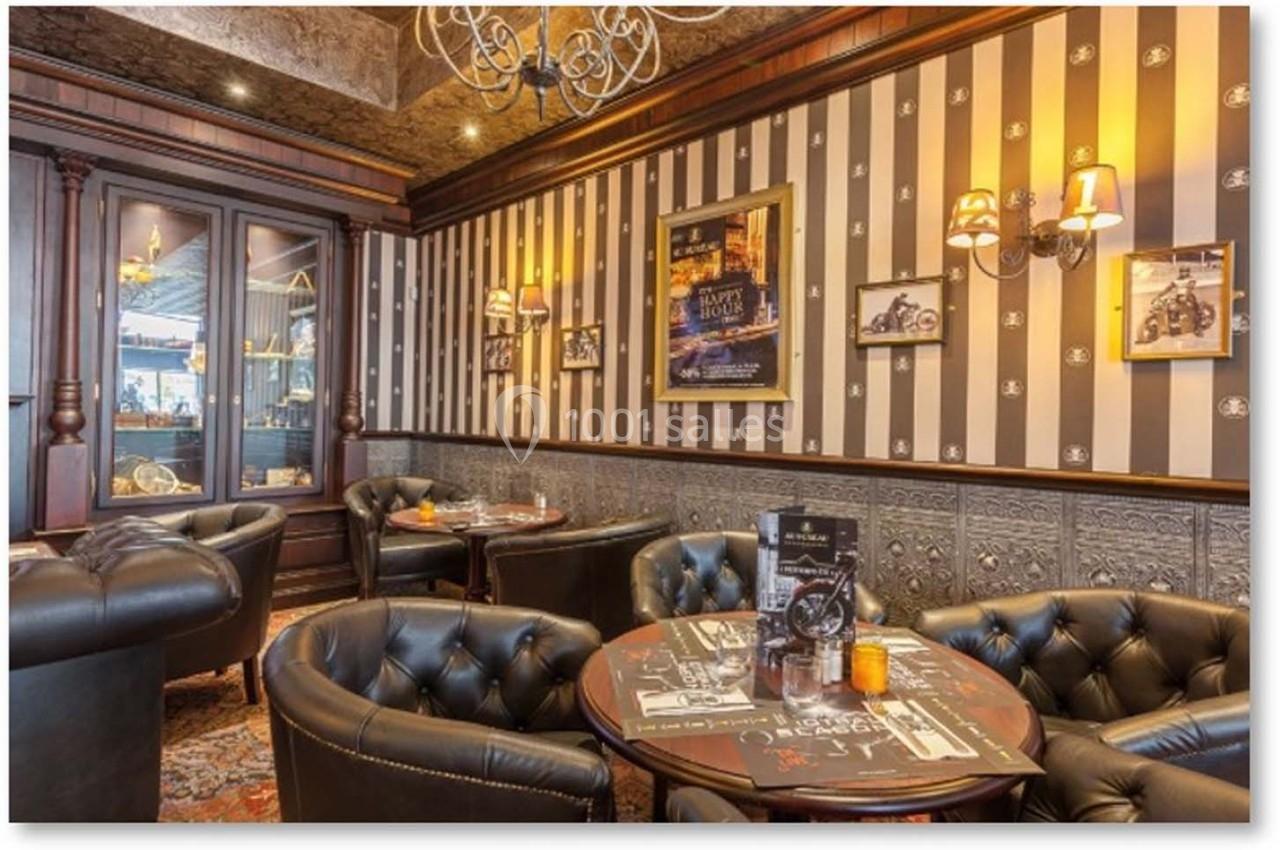 Salon élégant avec fauteuils en cuir noir, tables basses, murs rayés décorés et éclairage chaleureux.