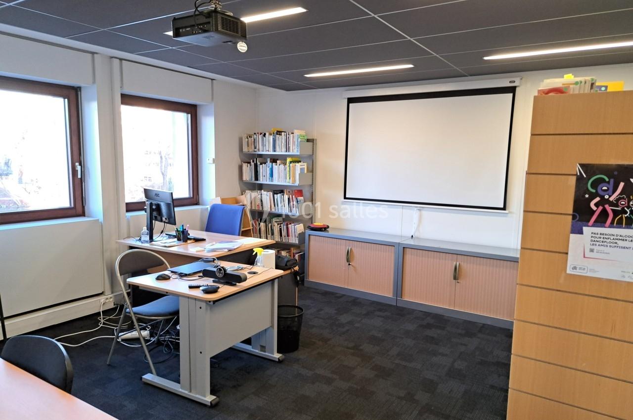 Salle de travail équipée d'un bureau avec ordinateur, étagères de livres, écran de projection et mobilier de rangement.