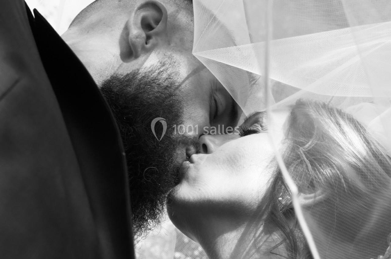 Un couple s'embrasse sous un voile de mariée, capturé en noir et blanc.