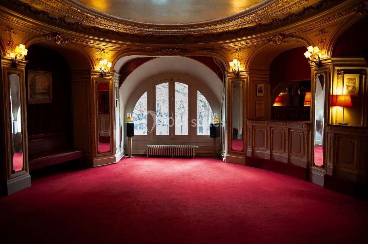 Intérieur d'un hall avec moquette rouge, miroirs, boiseries décoratives et grande fenêtre en arche.