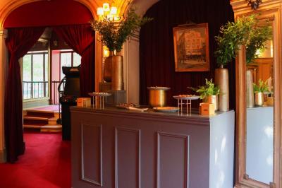 Miniature Espace restauration - Le Bar Entrée d'un théâtre avec comptoir rouge, escalier central, affiches murales et éclairage tamisé.