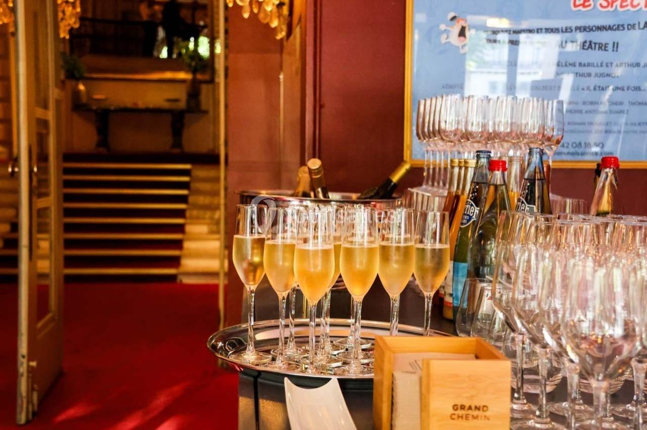 Flûtes de champagne alignées sur un plateau dans un hall élégant avec escalier en arrière-plan.