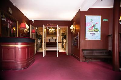 Miniature L'entrée Entrée d'un théâtre avec comptoir rouge, escalier central, affiches murales et éclairage tamisé.