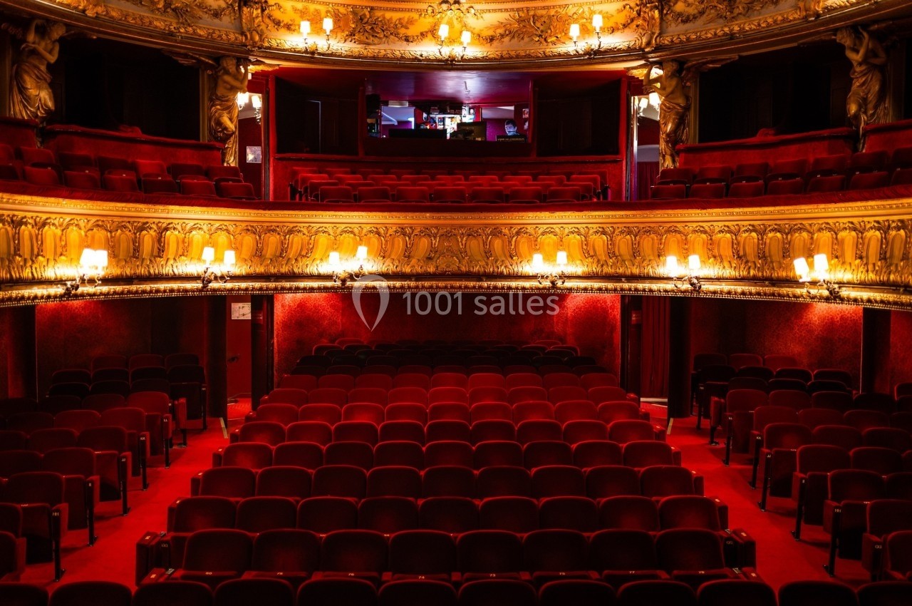 Salle de théâtre vide avec des sièges rouges, balcons ornés et éclairage chaleureux.